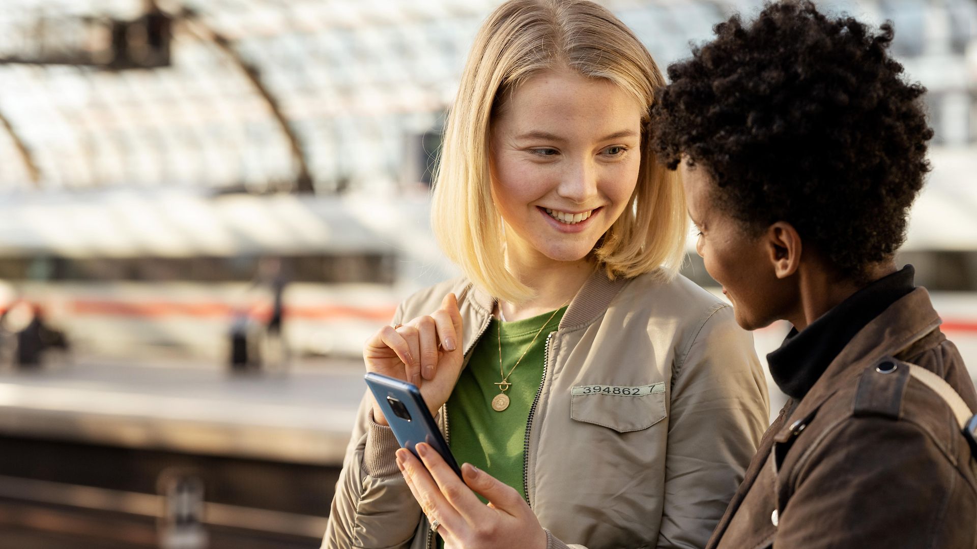 Zwei junge Frauen mit einem Handy auf dem Bahnsteig am Hauptbahnhof Berlin.